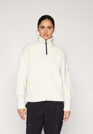 Fleecejakke i off-white med høy krage, frontglidelås og subtil teksturert mønster. Har lange ermer med tettsittende mansjetter.