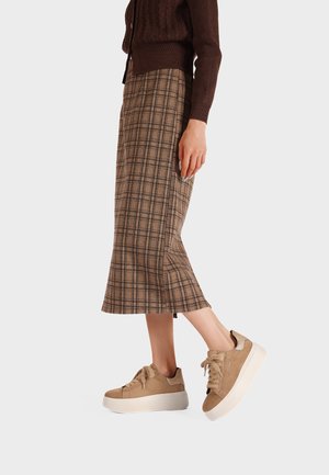Cardigan marrone abbinato a una gonna midi a quadri in tonalità beige e marrone scuro, e sneakers platform beige con dettagli in camoscio e pelle.
