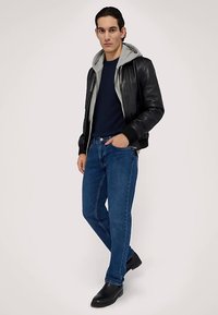 Giacca bomber in pelle nera con cappuccio grigio, t-shirt blu navy, jeans azzurri e stivali neri, che rappresenta un outfit casual su misura.