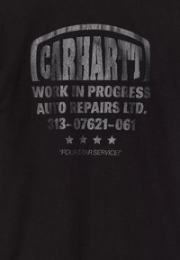 Czarna koszulka z srebrnym napisem: "CARHARTT WORK IN PROGRESS AUTO REPAIRS LTD." z numerem kontaktowym i pięciogwiazdkowym szczegółem poniżej.