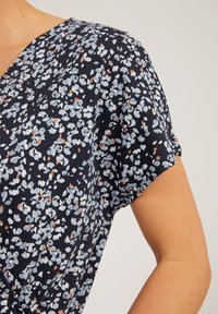 Góra w kwiatowy wzór w kolorze granatowym z jasnoniebieskimi i pomarańczowymi detalami. Miękki materiał, dekolt w serek, krótkie rękawy i luźny krój.