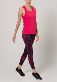 Fuksjowy bezrękawnik zestawiony z legginsami w czarne i różowe pasy. Modelka ma na sobie czarne sneakersy, prezentując sportowy, dopasowany wygląd.