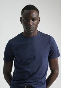 Camiseta de manga corta azul marino, con cuello redondo, fabricada en algodón, presenta un pequeño logo en el pecho, textura suave, diseño ajustado.