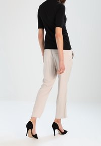 Sort kortærmet top parret med lyse beige tapered bukser og sorte højhælede sko. Glat stof med subtil struktur.