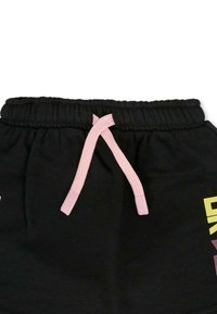 Pantalons de survêtement noirs avec une ceinture élastique, comportant un cordon de serrage rose et un texte graphique jaune sur le côté gauche.