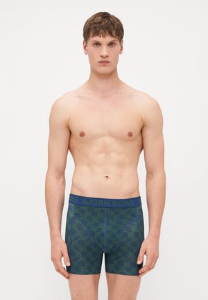 Culottes vertes et marine avec un motif de visages souriants répétitif, taille élastique avec "BJÖRN BORG" en texte bleu contrasté, conception ajustée.