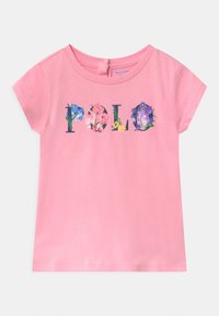 Camisa rosa de manga corta para niño pequeño con texto floral "Polo" en el pecho y un pequeño ojal con botón en la parte posterior del cuello.