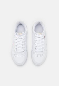 Bílé tenisky s hladkým koženým svrškem, perforovanou špičkou, plochými tkaničkami a minimálním brandingem s logem Reebok na jazyku.