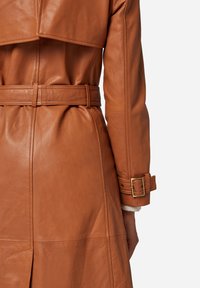 Brown leather trench coat with a belted waist, featuring a large collar, structured shoulders, and cuff accents. Smooth texture with stitching details.