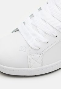 Hvit lær sneakers med teksturert overflate, med tykke hvite snørebånd, DC-logo og en slitesterk gummisåle.