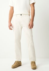 Pantaloni di cotone bianchi a taglio slim, con chiusura con bottone nero e tasche laterali, abbinati a scarpe in camoscio marrone chiaro.