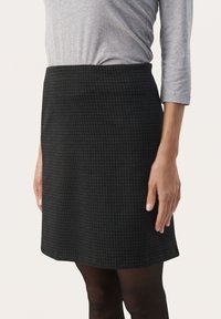 Jupe à motif écossais noir avec une taille cintrée, en tissu doux et de forme droite. Associée à un haut gris à manches longues.