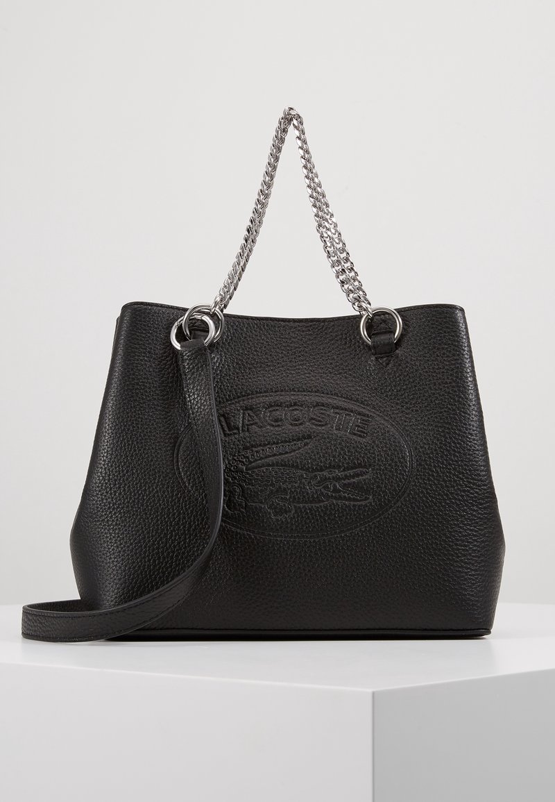 Sac seau en cuir noir à finition texturée, avec une bandoulière en chaîne argentée et un logo embossé. Comprend une bandoulière amovible.