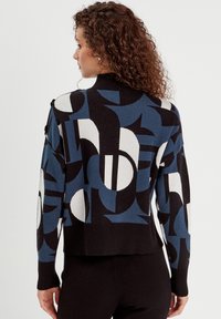 Maglione lavorato a maglia con un motivo geometrico in nero, blu e bianco. Design cropped con colletto e polsini a coste.