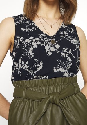 Top senza maniche blu navy con motivo floreale bianco, scollatura a V. Abbinato a una gonna di pelle verde oliva con cintura e dettaglio arricciato.