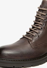 Stivale in pelle marrone con lacci, dotato di una tomaia testurizzata, con lacci beige a contrasto, punta arrotondata e una resistente suola in gomma nera.