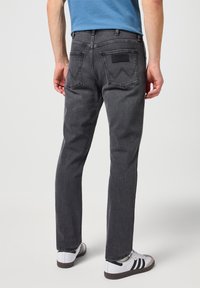 Jeans de mezclilla gris oscuro con un corte recto, que cuentan con dos bolsillos traseros y una etiqueta de cuero en la cinturilla. Usados con zapatillas blancas.