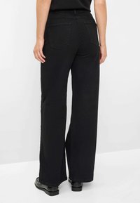 Jeans neri a gamba larga con vita alta, dotati di due tasche posteriori, cuciture decorative e una superficie liscia. Indossati con scarpe nere.