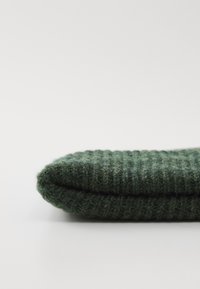 Gefalteter dunkelgrüner gestrickter Wollschal mit Rippstruktur auf weißem Hintergrund.