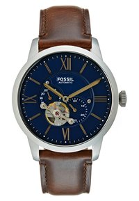 Reloj Fossil automático con esfera azul marino, caja de acero inoxidable plateado, correa de cuero marrón, marcadores de horas dorados y mecanismo de engranaje visible.