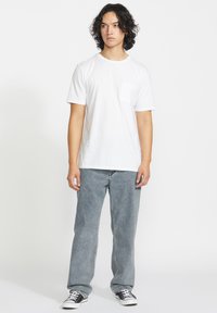 T-shirt blanche à manches courtes avec une poche poitrine, associée à un jean gris clair et des baskets noir et blanc. Design simple et coupe décontractée.