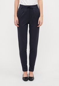 Navy tapered bukser i blødt stof har elastisk talje, plissee og elastiske manchetter. Sætter det sammen med sorte flade sko for et fuldendt look.