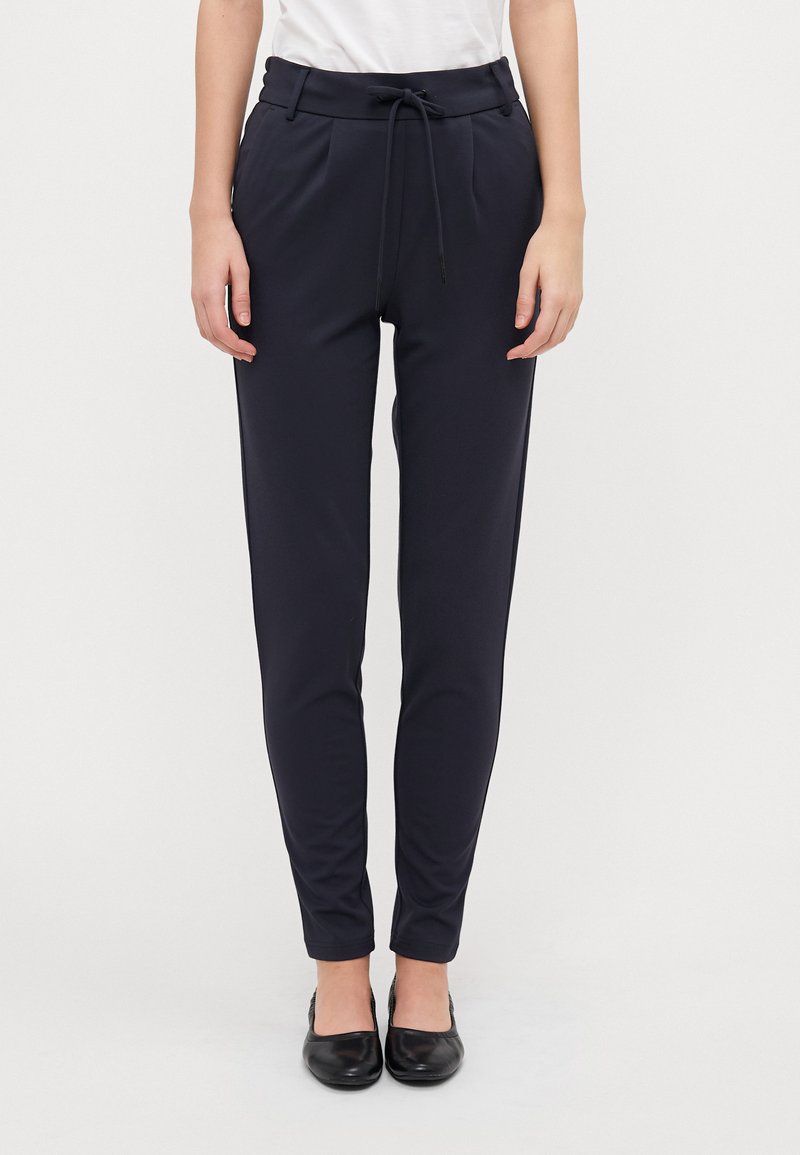 Navy tapered bukser i blødt stof har elastisk talje, plissee og elastiske manchetter. Sætter det sammen med sorte flade sko for et fuldendt look.
