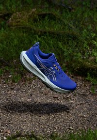 Μπλε αθλητικό παπούτσι με υφή στην επάνω πλευρά, μαξιλαρωμένη σόλα και χρυσές λεπτομέρειες. Διαθέτει ελαφριά σχεδίαση και αναπνεύσιμο υλικό.