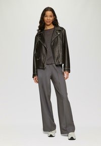 Schwarze Lederbikerjacke mit silbernen Reißverschlüssen, kombiniert mit einem grauen strukturierten Pullover und grauen weit geschnittenen Hosen. Weiße Sneaker runden den Look ab.