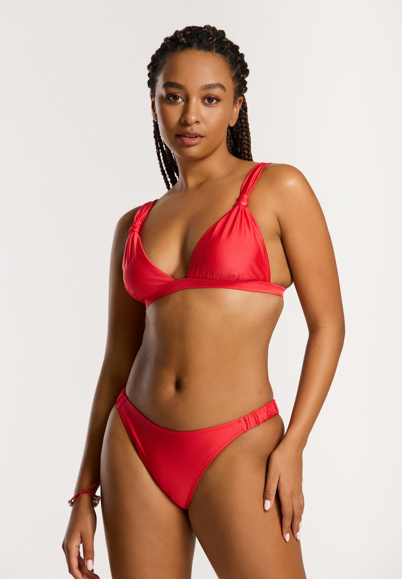 Piros bikini, háromszög alakú toppal, kötött pántokkal és alacsony derekú alsó résszel. Sima textúra, minimális design.
