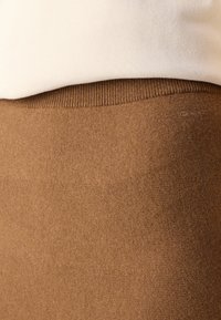 Brun texturerad stickad tyg med en ribbad midja och ett slitstarkt vitt överlager. Enkel design utan synliga mönster eller metalldelar.