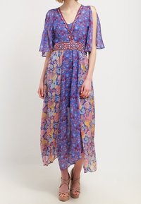 Maxi šaty z lehké modré tkaniny, s květinovými a paisley vzory, V-výstřihem a krátkými volánkovými rukávy. Doplňují je červený pásek.