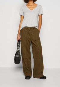 Grijze korte mouw T-shirt met V-hals, gecombineerd met olijfgroene broek met wijde pijpen. Zwarte tas met studs als accent. Soepele stof en ontspannen pasvorm.