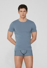 Camiseta gris ajustada de manga corta y textura suave, combinada con pantalones cortos tipo tronco a juego que presentan detalles de costura en contraste.