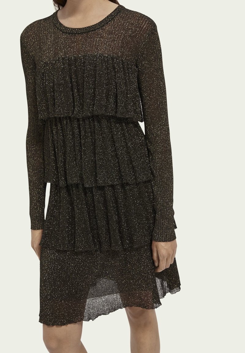 Schwarzes Glitzerkleid mit langen Ärmeln, gestuften Rüschen am Oberteil und Rock sowie einer leicht durchsichtigen Textur. Der Saum fällt hinten ab.