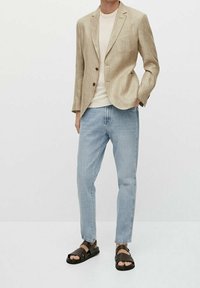 Jasnobeżowa lniana marynarka na dwa guziki, w zestawieniu z kremowym T-shirtem, jasnoniebieskimi zwężanymi jeansami i czarnymi sandałami na paski.