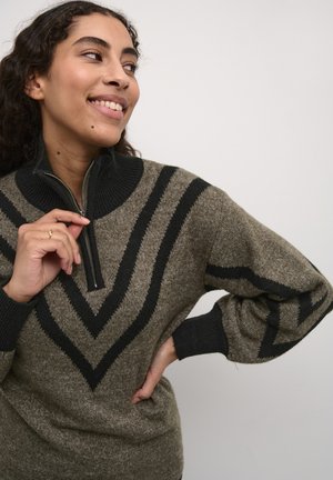 Pull en maille vert olive avec un motif en chevrons noirs. Il dispose d'un col zippé et de poignets côtelés. Texture douce avec une coupe décontractée.