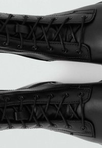 Botas de tobillo de cuero negro con puntera redonda, con un diseño de cordones y ojetes de metal. Textura suave con detalles de costura minimalista.