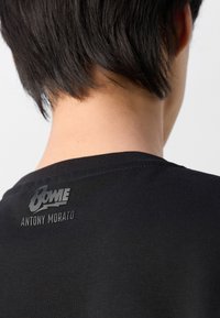 Crna pamučna majica s okruglim izrezom. Na leđima se nalazi uzdignuti print loga s natpisom "BOWIE" iznad "ANTONY MORATO."
