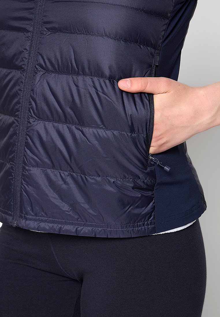 Gilet en bleu marine, isolé, avec des sections matelassées, une poche zippée sur le côté et une finition lisse. Présente un panneau contrastant en bleu marine en dessous.