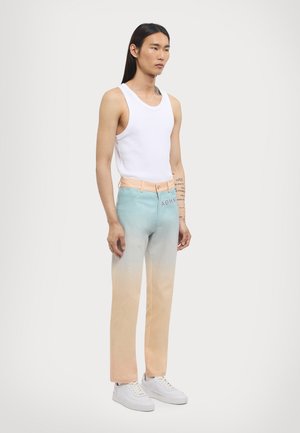 Top alb fără mâneci cu gradient de la albastru deschis la piersiciu, pantaloni din denim drept, cu logo pe buzunar și adidași albi cu tălpi texturate.