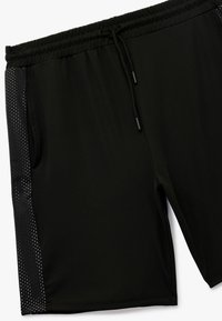 Sorte sportsshorts med elastisk talje, snøre lukning og sidelapper med et perforeret design for åndbarhed.