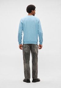 Sweatshirt azul claro com decote redondo e punhos canelados, combinado com jeans cinza com um aspeto desbotado e bolsos traseiros. Sapatos pretos visíveis.