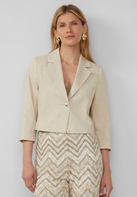 Beige cropped blazer met driekwart mouwen, met opgestikte kleppen en een enkele knoopsluiting, gecombineerd met beige broek met een patroon.