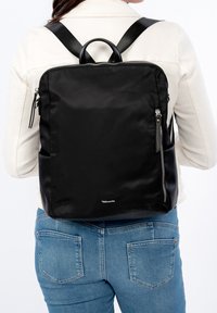 Mochila negra de nailon con una textura suave, que presenta correas dobles para los hombros, un asa superior y bolsillos laterales con cremallera.