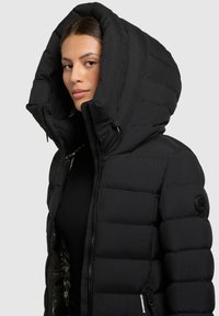 Must mustern vere, suur kapuuts, diivanitekstiiliga muster, tõmblukuga sulgemine ja küljetaskud. Vasakul käel on logopatch.