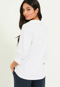 Weißes, langärmliges Hemd mit Knopfleiste und Kragen, mit hochgekrempelten Ärmeln und einem lässigen Schnitt. Strukturierter Stoff, lässiges Design.