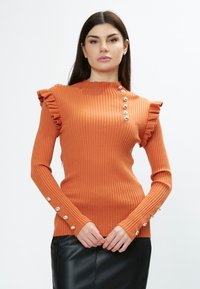 Ribbede, langærmede orange top med flæse accenter på skuldrene og sølvknapdetaljer langs skuldrene og manchetterne. Strukturstrik materiale.