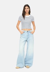 Bílý crop top s námořnickými pruhy; spárován se světle modrými širokými džíny. Výrazné detaily zahrnují přiléhavý střih a vysoký pas.
