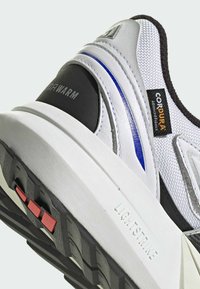 White and black athletic shoe with a textured fabric upper, blue accents, a thick white midsole, and a patterned rubber outsole.